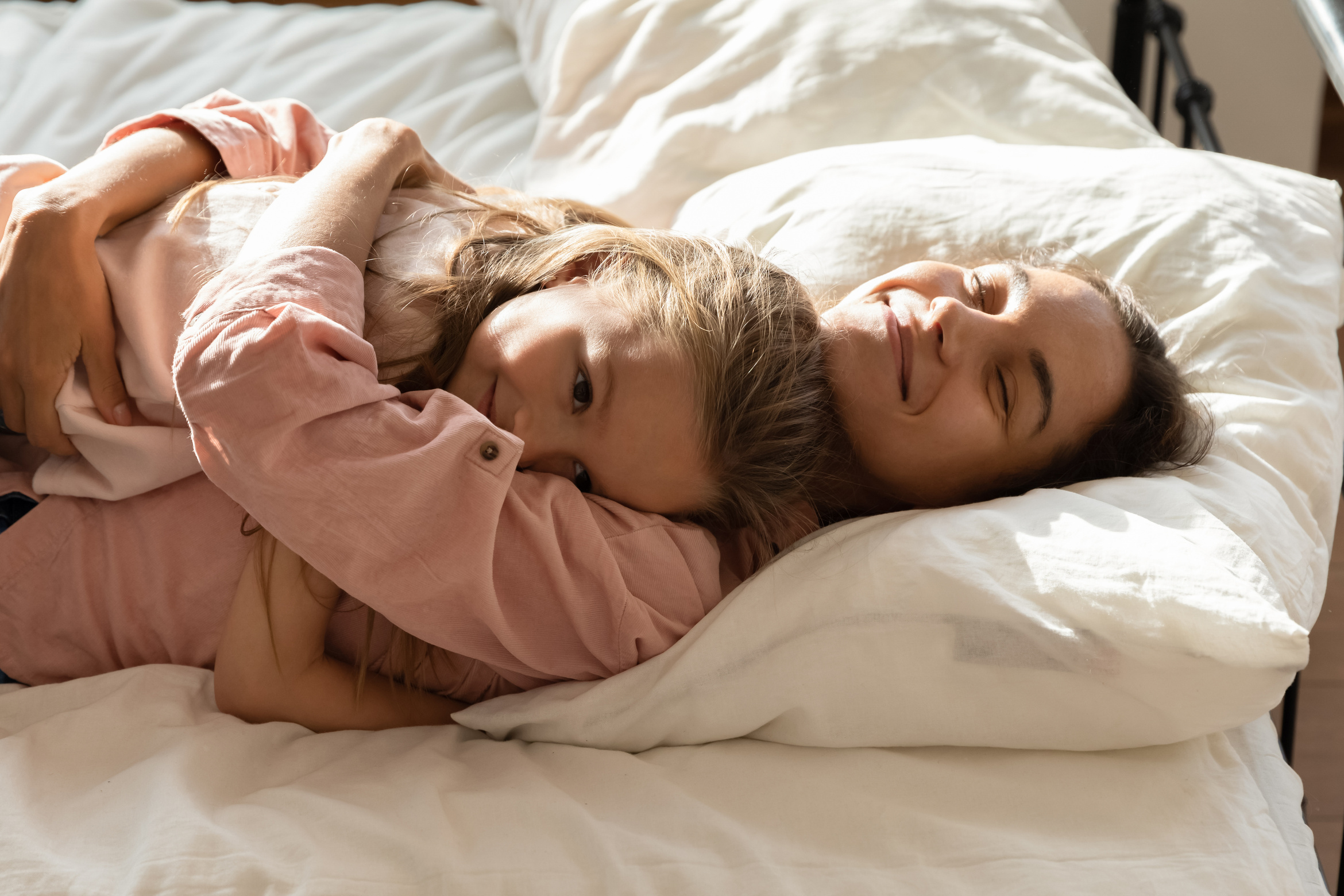 Loving mum cuddle relaxing in bed with little daughter